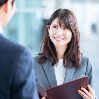 バインダーをもった女性社員が笑顔で話している様子