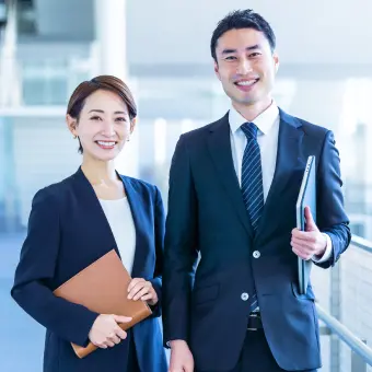 手帳を持った女性社員とノートパソコンをもった男性社員が笑っている様子